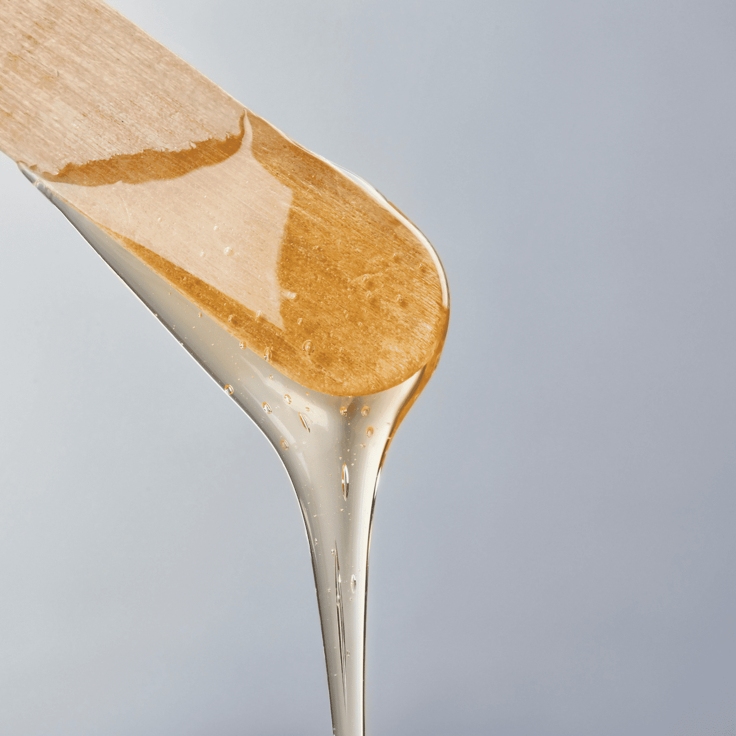 Wooden spatula with honey dripping against a light background.
