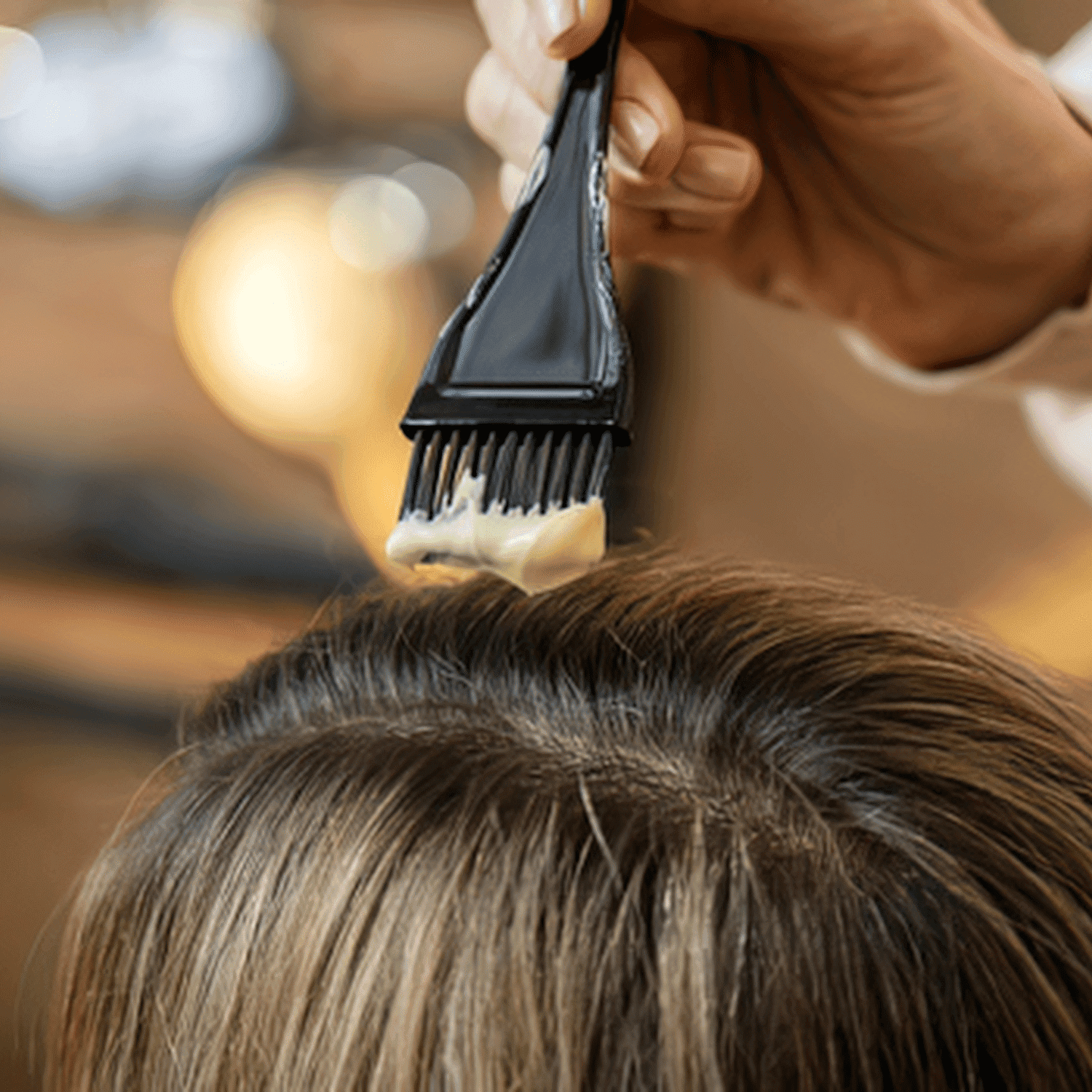 Hair dye being applied to strands of hair with a brush in a salon setting.