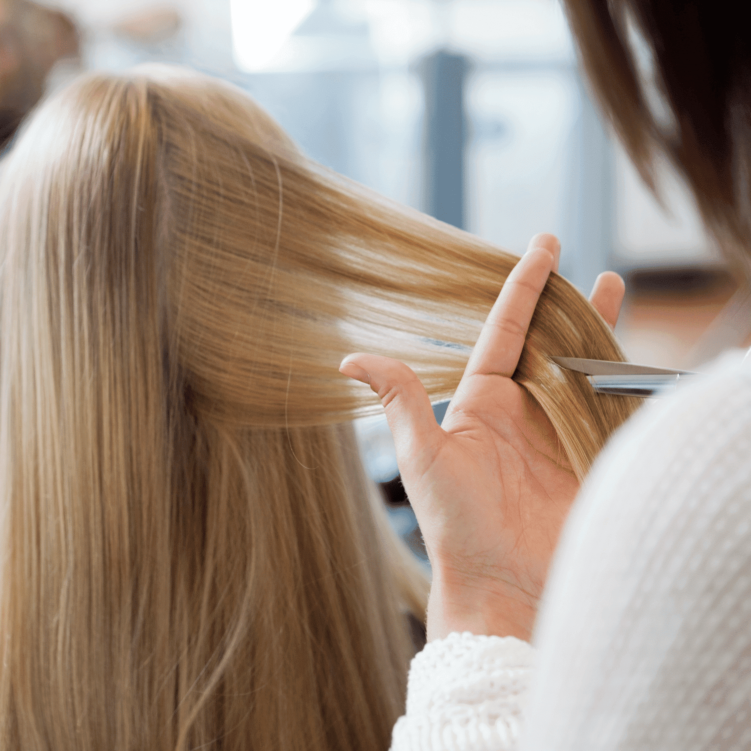 Person cutting long blonde hair with scissors in a salon setting.